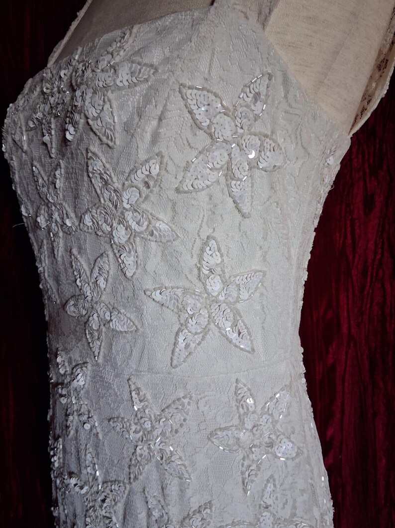 Puede incluir: Vestido color marfil con un dise&ntilde;o floral. El vestido presenta un corpi&ntilde;o ajustado y una delicada capa de encaje. El dise&ntilde;o floral est&aacute; adornado con lentejuelas, a&ntilde;adiendo un toque de brillo. El vestido tiene una silueta simple y elegante, perfecto para ocasiones especiales.