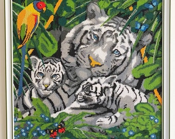 May include: A white tiger with two cubs in a lush green jungle setting. The tiger is lying down with its cubs nestled beside it. A colorful bird is perched on a branch in the background.