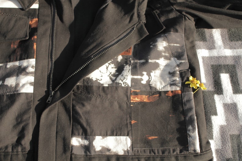 Puede incluir: Una chaqueta negra con cierre de cremallera y un dise&ntilde;o de patchwork. Los parches est&aacute;n hechos de diferentes telas y tienen una variedad de colores y patrones. La chaqueta tiene un bolsillo en el lado derecho.