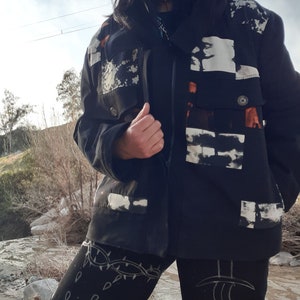 Puede incluir: Una chaqueta negra con dise&ntilde;os abstractos blancos y naranjas. La chaqueta tiene una cremallera y un cuello. La persona que lleva la chaqueta tambi&eacute;n lleva leggings negros con dise&ntilde;os blancos.