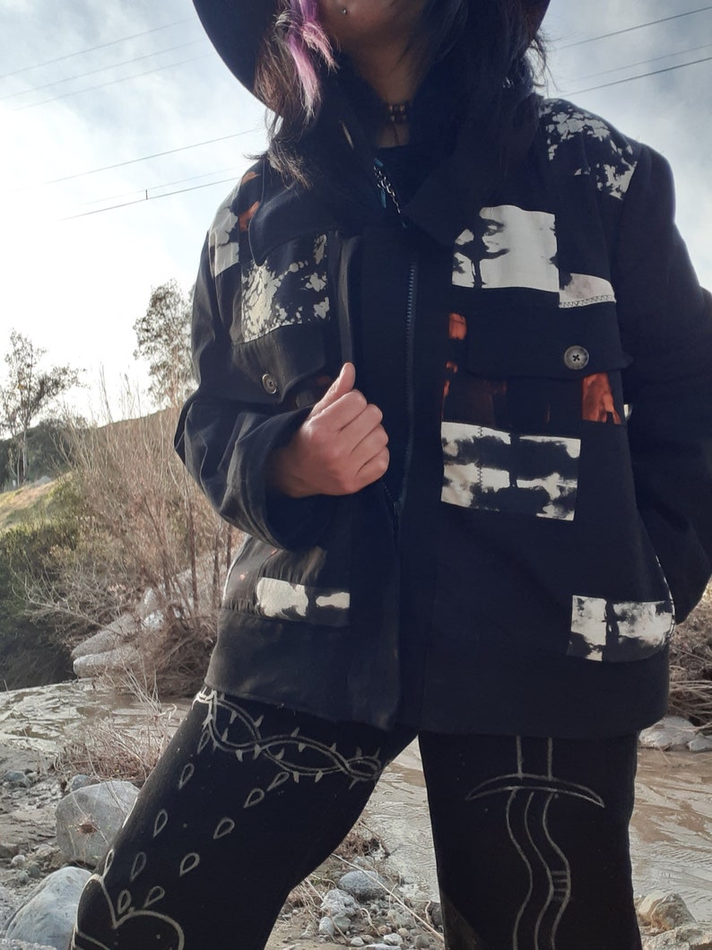 Puede incluir: Una chaqueta negra con dise&ntilde;os abstractos blancos y naranjas. La chaqueta tiene una cremallera y un cuello. La persona que lleva la chaqueta tambi&eacute;n lleva leggings negros con dise&ntilde;os blancos.