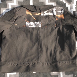 Puede incluir: Una chaqueta negra con un dise&ntilde;o de patchwork en la espalda. Los parches est&aacute;n hechos de diferentes telas y tienen un esquema de color marr&oacute;n, blanco y negro.