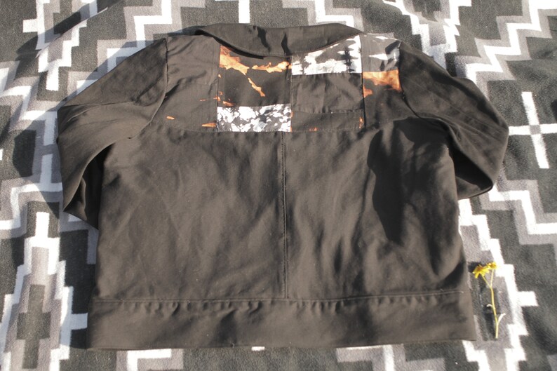 Puede incluir: Una chaqueta negra con un dise&ntilde;o de patchwork en la espalda. Los parches est&aacute;n hechos de diferentes telas y tienen un esquema de color marr&oacute;n, blanco y negro.
