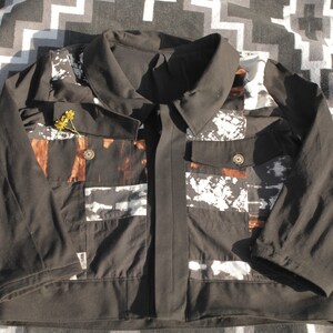 Puede incluir: Una chaqueta negra con un estampado abstracto blanco y marr&oacute;n. La chaqueta tiene cuello, cierre de cremallera y dos bolsillos.