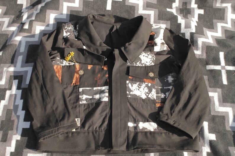 Puede incluir: Una chaqueta negra con un estampado abstracto blanco y marr&oacute;n. La chaqueta tiene cuello, cierre de cremallera y dos bolsillos.