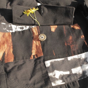 Puede incluir: Una chaqueta negra con un dise&ntilde;o de patchwork marr&oacute;n y blanco. La chaqueta tiene un cierre de bot&oacute;n &uacute;nico y una flor metida en el cuello.