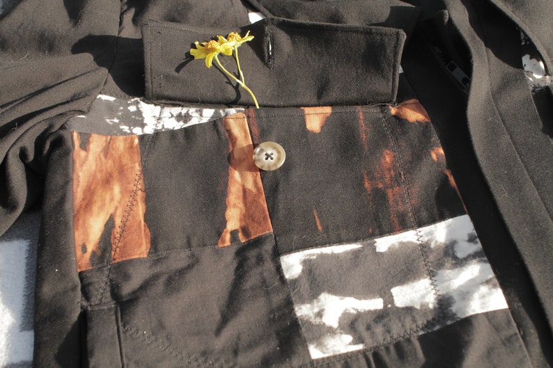 Puede incluir: Una chaqueta negra con un dise&ntilde;o de patchwork marr&oacute;n y blanco. La chaqueta tiene un cierre de bot&oacute;n &uacute;nico y una flor metida en el cuello.