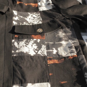 Puede incluir: Camisa de algod&oacute;n negra con un dise&ntilde;o de patchwork con acentos blancos y marrones. La camisa tiene un cierre de bot&oacute;n y un bolsillo en el lado izquierdo.