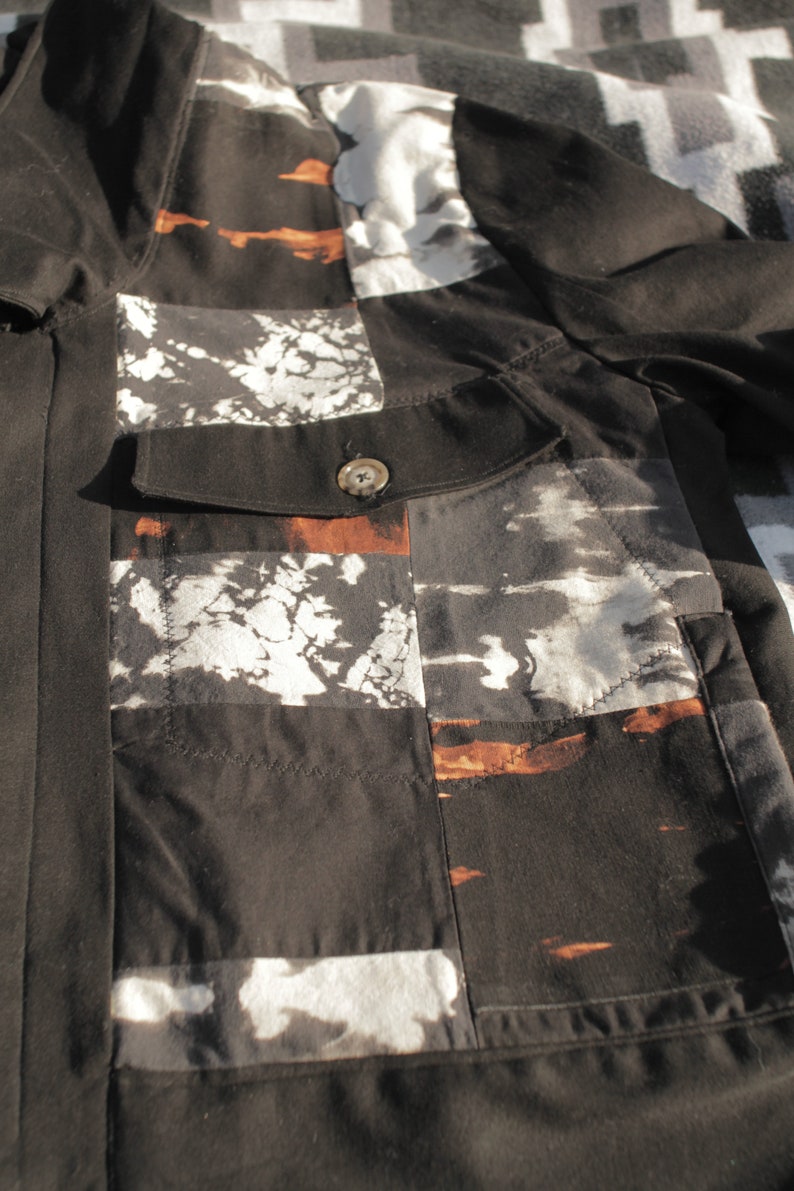 Puede incluir: Camisa de algod&oacute;n negra con un dise&ntilde;o de patchwork con acentos blancos y marrones. La camisa tiene un cierre de bot&oacute;n y un bolsillo en el lado izquierdo.