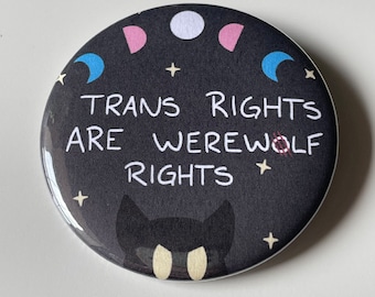 May include: A black button with a white background featuring a black cat with yellow eyes, a crescent moon, and the text "Trans Rights Are Werewolf Rights".