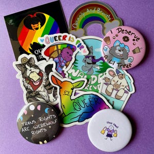 May include: A collection of colorful stickers and buttons with LGBTQ+ themes. The stickers feature cartoon animals, rainbows, and text like "Queer is for" and "Openly and Bravely." Buttons include "Trans Rights are Werewolf Rights" and "I Deserve a Lil Treat."