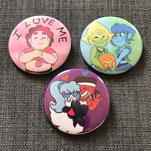 May include: Three round button pins with colorful cartoon characters. The first pin is pink with a pink character with the text "I LOVE ME". The second pin is blue and green with two characters holding a pumpkin. The third pin is purple with two characters hugging.