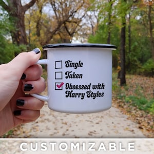 K&ouml;nnte beinhalten: Wei&szlig;e Email Tasse mit schwarzem Rand und Henkel. Die Tasse hat eine Checkliste mit drei Optionen: Single, Taken, Obsessed with Harry Styles. Die dritte Option ist angekreuzt.