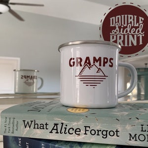 K&ouml;nnte beinhalten: Wei&szlig;e Emaille-Campingtasse mit einer roten Berggrafik und dem Text "GRAMPS" auf der Vorderseite. Die Tasse hat einen silbernen Rand und einen Griff. Der Text "DOUBLE SIDED PRINT" ist in einem roten Kreis im Hintergrund sichtbar.
