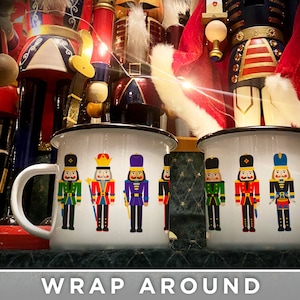 May include: Two white enamel mugs with black rims. Both mugs feature a wrap-around design of colorful nutcracker soldiers. One mug has the text "YOUR NAME" on the side.