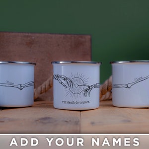 May include: Two white enamel camping mugs with black skeletal hand designs. The mug on the left has the text "Name" and the mug on the right has the text "Name" and "Till death do us part."