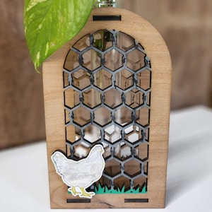 Op de afbeelding: Houten vaas met een kipontwerp en een doorzichtige glazen buis voor een plant. De vaas heeft een gaasontwerp en een groen grasontwerp aan de onderkant.