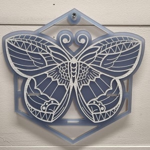Op de afbeelding: Een witte vlinder met ingewikkelde details is uitgesneden uit een lichtblauw zeshoekig stuk acryl.