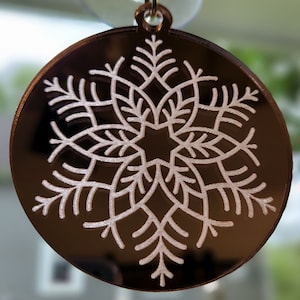 Op de afbeelding: Een ronde, bruine, gespiegelde hanger met een wit sneeuwvlokkenpatroon. De hanger heeft een lus aan de bovenkant om op te hangen.