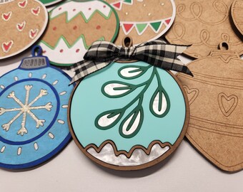 May include: A set of six unfinished wooden ornaments, including a blue ornament with a snowflake design, a teal ornament with a green leaf design, and four brown ornaments with various designs.