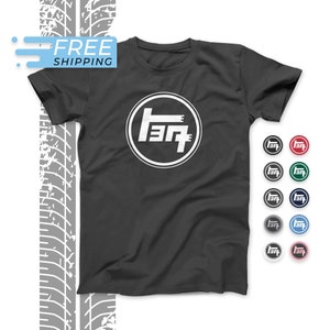 Może przedstawiać: Szary t-shirt z białym logo Toyoty z przodu. Logo to okrąg z napisem "Toyota" w japońskich znakach. Koszulka dostępna jest w różnych kolorach.