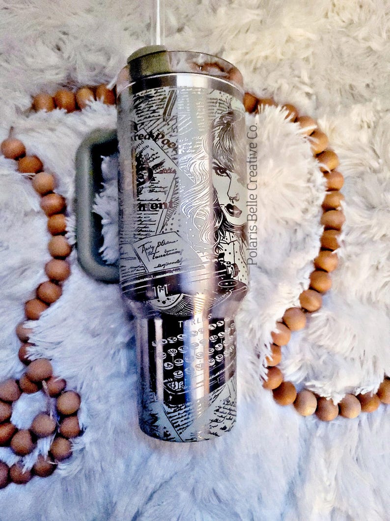 Puede incluir: Un vaso de acero inoxidable con un dise&ntilde;o detallado que presenta el rostro de una mujer, teclas de m&aacute;quina de escribir y recortes de peri&oacute;dicos. El vaso tiene un asa y una tapa. El texto "Polaris Belle Creative Co." es visible.