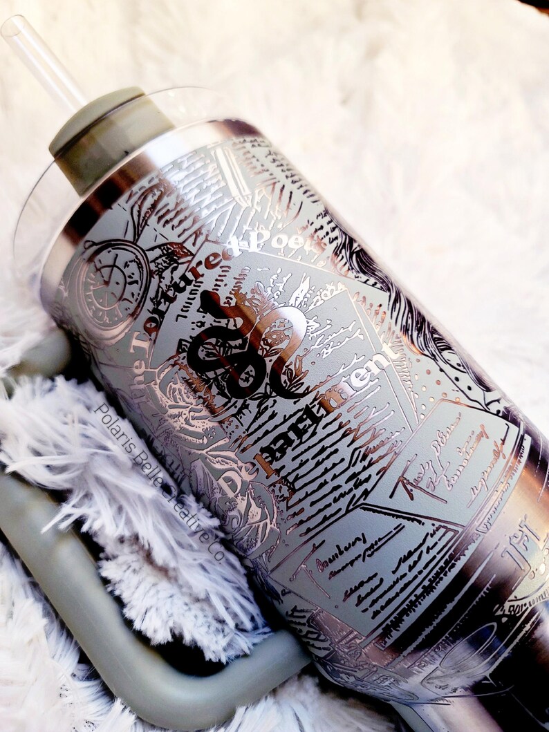 Puede incluir: Un vaso de acero inoxidable con pajita y tapa transparente. El vaso presenta un dise&ntilde;o detallado con texto e ilustraciones en plata y negro. El texto incluye las palabras "Torture Me Poet" y "Basement".