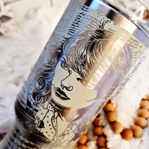 Puede incluir: Un vaso plateado con un retrato grabado en blanco y negro de una mujer. El dise&ntilde;o se encuentra sobre un fondo de texto. Las palabras "Polaris Belle Creative Co." est&aacute;n impresas en el lateral del vaso. El vaso es cil&iacute;ndrico.