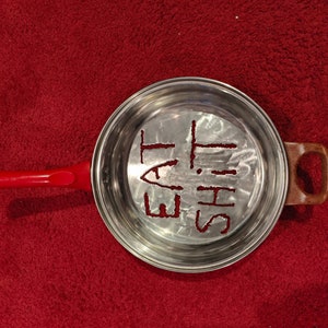Puede incluir: Una sart&eacute;n de plata con un mango rojo. La sart&eacute;n tiene las palabras "Eat This" rayadas en el fondo.