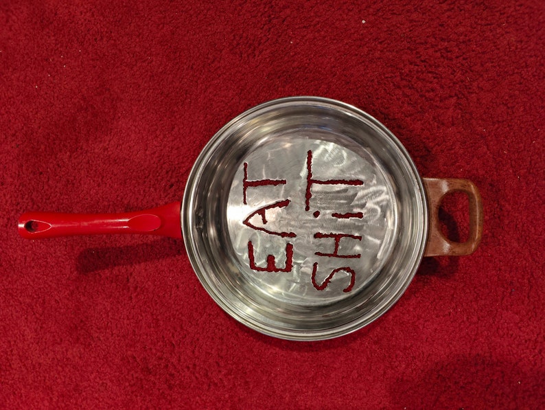 Puede incluir: Una sart&eacute;n de plata con un mango rojo. La sart&eacute;n tiene las palabras "Eat This" rayadas en el fondo.