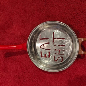 Puede incluir: Una sart&eacute;n de plata con un mango rojo. La sart&eacute;n tiene las palabras "Eat This" grabadas en el fondo.
