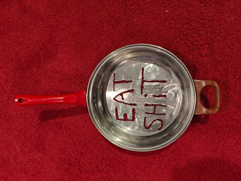 Puede incluir: Una sart&eacute;n de plata con un mango rojo. La sart&eacute;n tiene las palabras "Eat This" grabadas en el fondo.