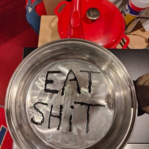 Puede incluir: Una sart&eacute;n de metal plateado con las palabras "EAT SHIT" grabadas en el fondo.