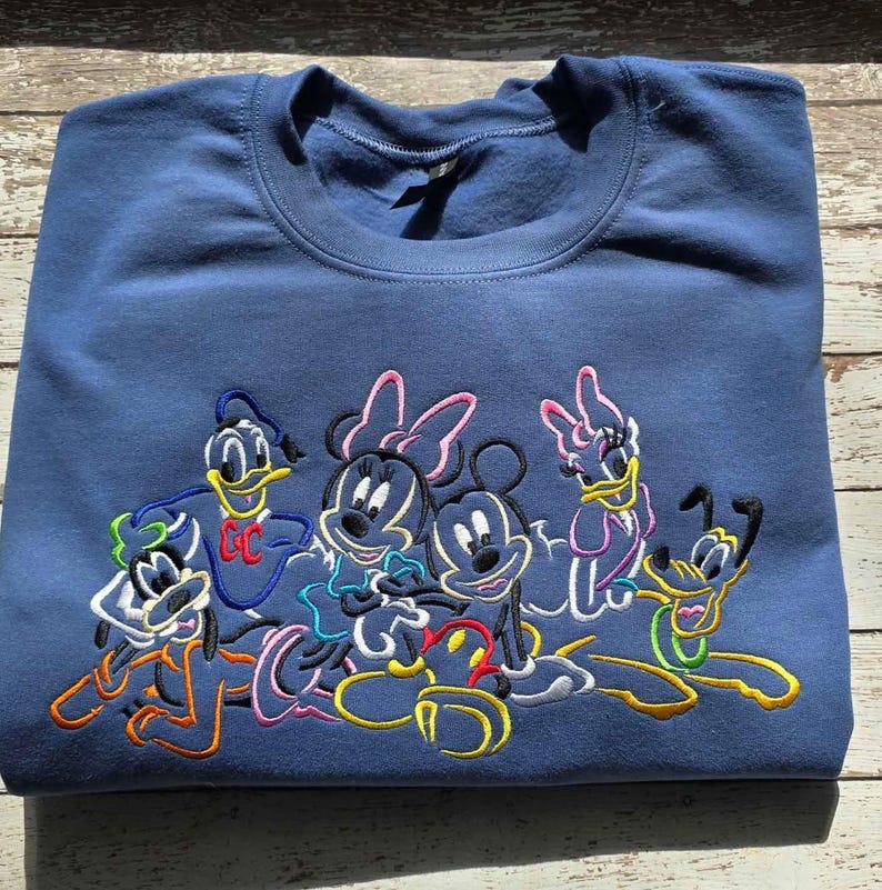 May include: A navy blue sweatshirt featuring an embroidered design of Disney characters, including Mickey and Minnie Mouse, Donald Duck, Daisy Duck, and Pluto. The characters are outlined in various colors.