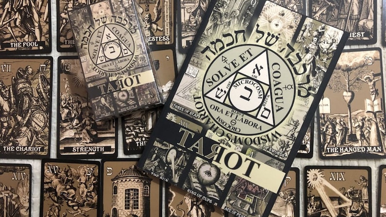 May include: A black and white tarot deck with a black box and a guidebook. The guidebook has a black cover with a white triangle and the words "Solve et Coagula" in Hebrew. The cards feature black and white illustrations of tarot symbols.