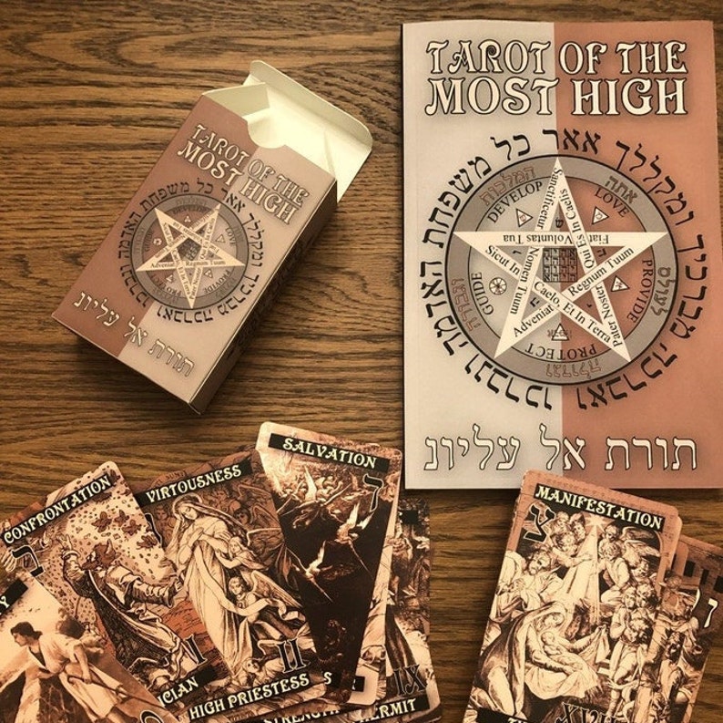 Puede incluir: Una caja de baraja de tarot con el t&iacute;tulo "Tarot of the Most High" en hebreo e ingl&eacute;s. La caja es marr&oacute;n con una estrella dorada y texto en hebreo. Las cartas est&aacute;n extendidas sobre una superficie de madera. Las cartas presentan ilustraciones de personas y escenas.
