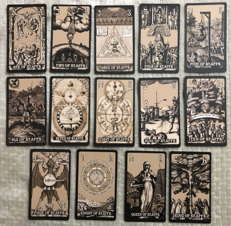May include: A set of 14 tarot cards featuring black and white illustrations on a beige background. The cards depict various scenes and symbols, including a man with a staff, a woman with a crown, and a tree with a hanging figure. The cards are numbered from 1 to 10 and include the Page, Knight, Queen, and King of Staffs.