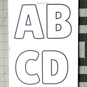 May include: White rectangular sticker sheet with the letters A, B, C, and D in a dark gray outline font. The letters are in a bold, rounded style. The text "@saffron.lane" is in the upper right corner.