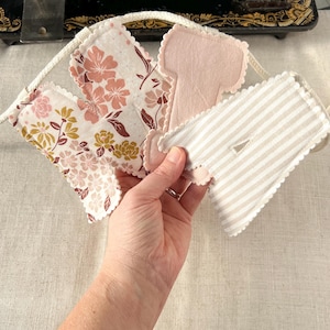 May include: A handmade fabric banner with various patterned pieces. The banner includes floral prints in pink and gold, solid pink felt, and a striped design. The edges are scalloped, and the banner is strung on a white rope.