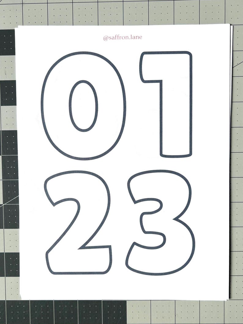 May include: White paper with the numbers 0, 1, 2, and 3 outlined in dark gray. The numbers are in a bold, rounded font. The text "@saffron.lane" is in the top right corner.
