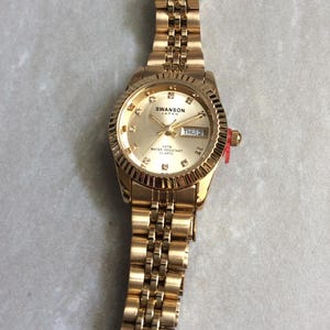 Reloj SWANSON dorado para mujer, esfera redonda dorada, horas de cristal, día y fecha en correa de oro enlazada, reloj vintage nuevo sin usar. ¡Belleza!