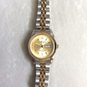SWANSON Damenuhr rundes goldenes Zifferblatt Index Stundenmarkierungen Tag & Datum auf Gold Linked Band Neuer unbenutzter Vintage Artikel!