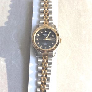 Reloj para mujer SWANSON, esfera redonda negra, marcadores de hora de cristal, indicador de día y fecha, todo en una correa unida de dos tonos, nuevo, vintage, sin usar, WR5ATM.