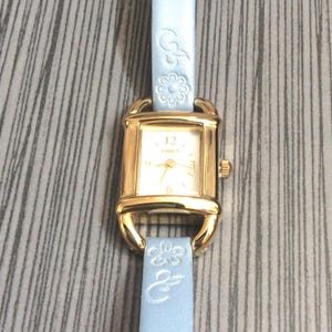 Reloj Timex rectangular dorado para mujer, esfera plateada, marcadores de hora árabes e índices dorados en una correa de cuero azul con diseño floral. ¡Reloj vintage sin usar!