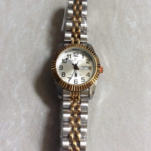 MONTRES CARLO Damenuhr mit einem runden silbernen Zifferblatt, schwarz nummerierten Stunden mit Wochentag und Datum, alle auf einem zweifarbigen verknüpften Band