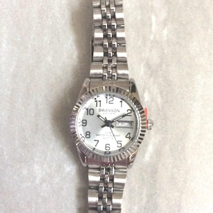 Reloj Swanson para mujer, plateado, esfera redonda plateada, horas y fecha numeradas en negro sobre una correa de eslabones plateados. ¡Reloj vintage nuevo sin usar!