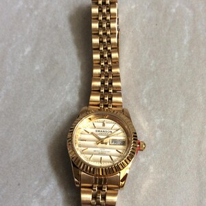 SWANSON Damen-Golduhr mit rundem goldenem Zifferblatt Index Stunden, Wochentag und Datum auf einem vergoldeten Band Neue unbenutzte Vintage Uhr WR 5ATM bewertet!