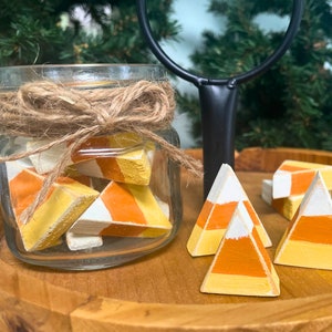 May include: A glass jar filled with small wooden candy corn decorations, tied with twine.  Four larger wooden candy corn decorations are on a wooden tiered tray.
