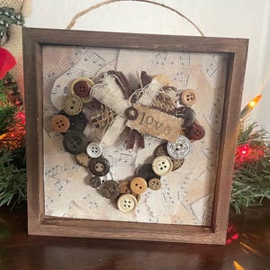 May include: A framed heart-shaped artwork made of buttons and burlap with a "love" tag on a background of sheet music.