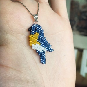 May include: A beaded bird pendant necklace with a blue, yellow and white design. The pendant is attached to a silver chain.
